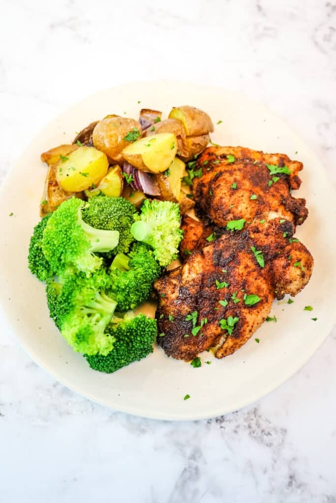 Roasted chicken thighs and potatoes on a plate with sauteed broccoli.