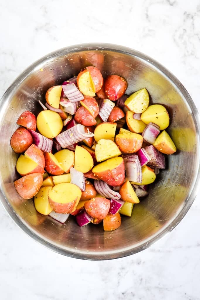 Quartered red potatoes and red onions in a mixing bowl, coated with olive oil and seasoning.