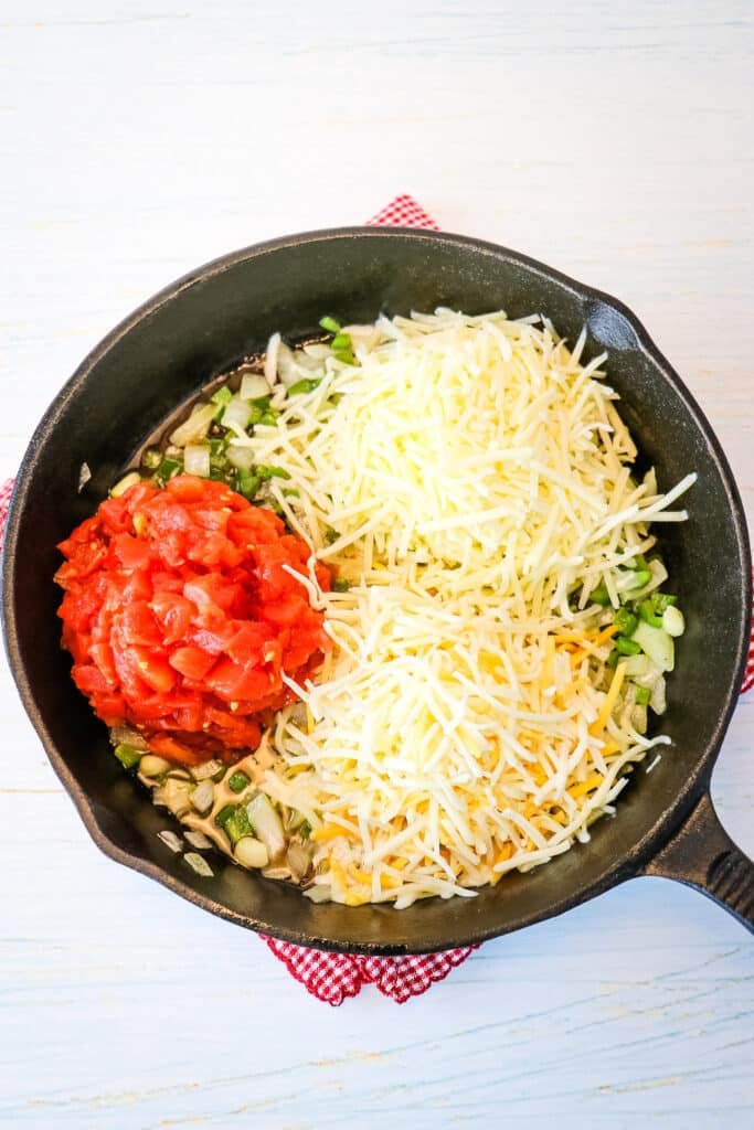 Tomatoes and shredded cheeses are added to the skillet to make white queso dip.