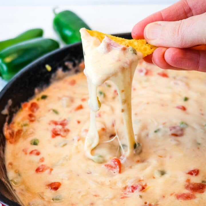White queso dip being served from a cast iron skillet with chip being dipped.