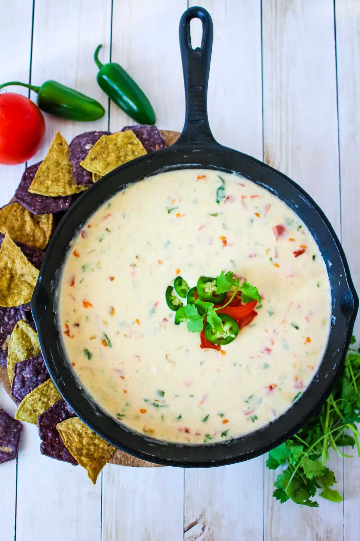 Homemade white queso dip in a cast iron skillet, with tortilla chips being served on the side.