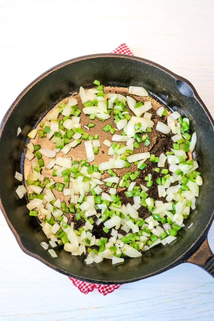 Diced onion and jalapeno in a cast iron skillet being sauteed for white queso dip.