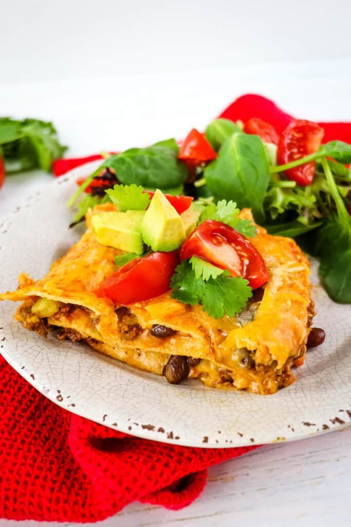 Slice of beef enchilada casserole on a plate served with a green salad.