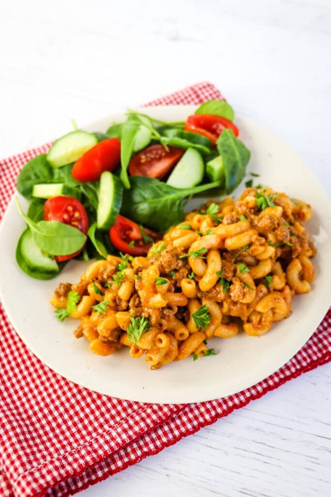 Serving of cheeseburger macaroni on a plate with a green salad on the side.