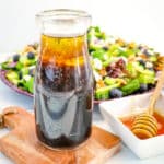 Jar of honey balsamic vinaigrette in a jar with honey on the side and salad in the background.