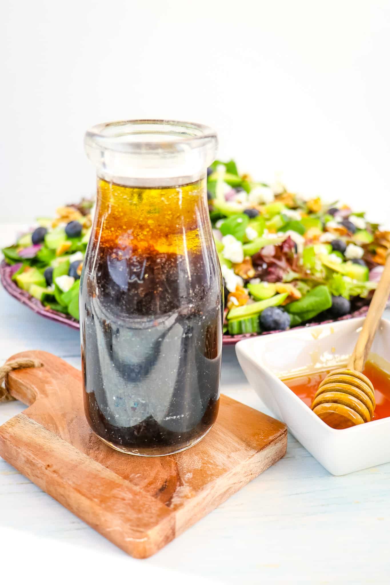 Jar of honey balsamic vinaigrette in a jar with honey on the side and salad in the background.