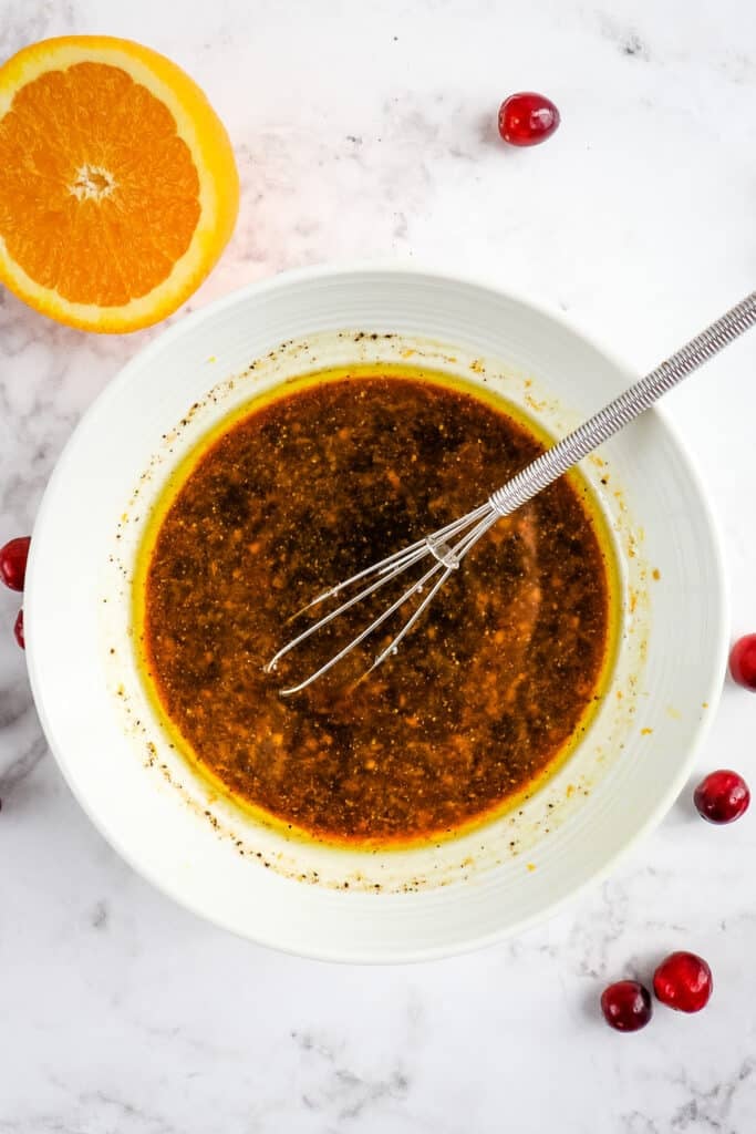 Honey balsamic vinaigrette in a bowl with a mini whisk and half orange on the side.