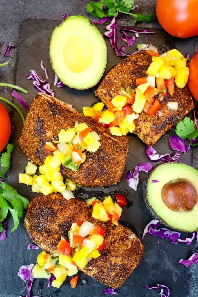 Mahi mahi air fryer filets topped with pineapple mango salsa with avocado, cilantro and tomato on the side.