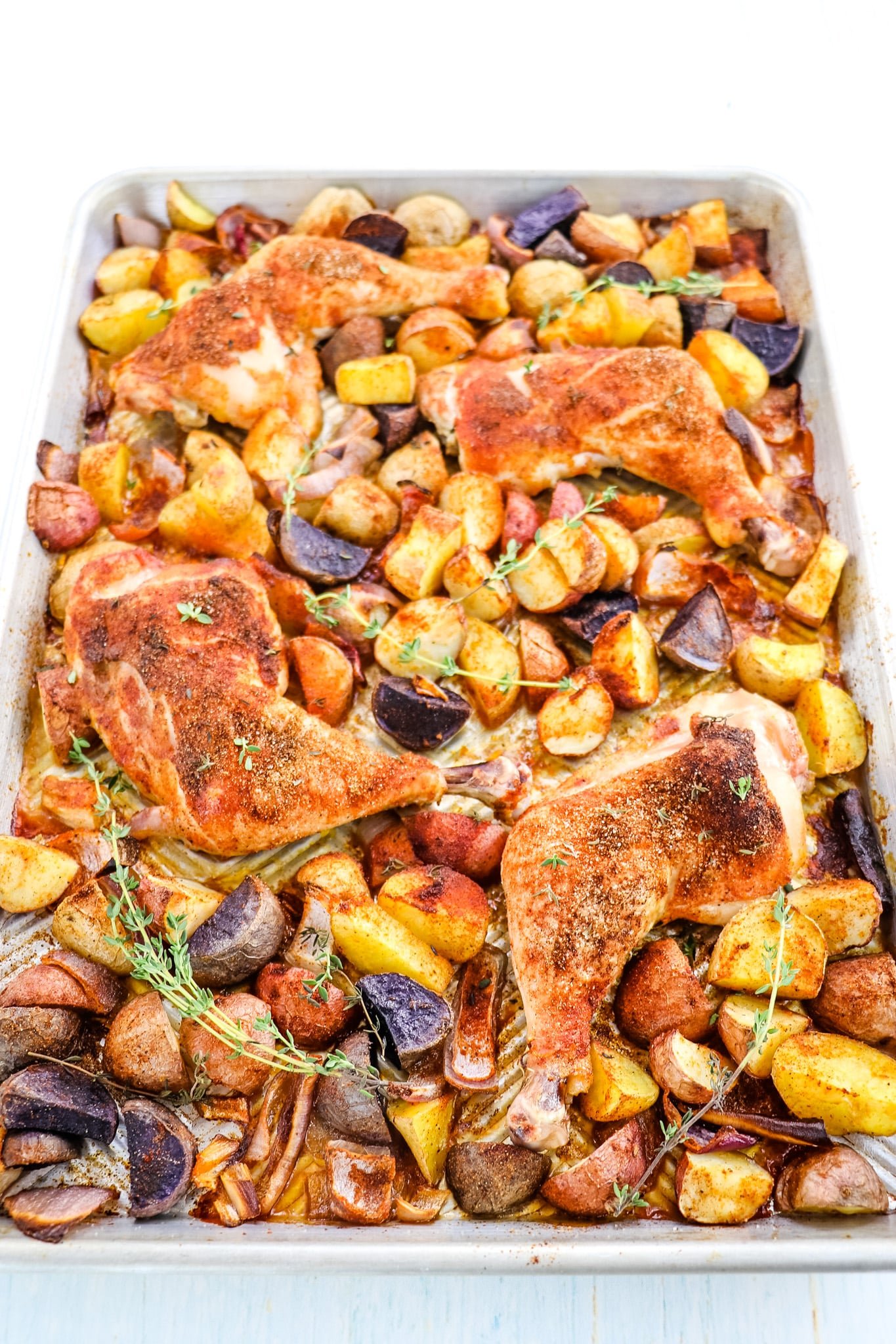 Oven baked chicken quarters with potatoes and onions on a sheet pan.