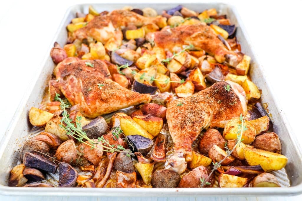 Oven baked chicken quarters on a sheet pan with potatoes and onions.