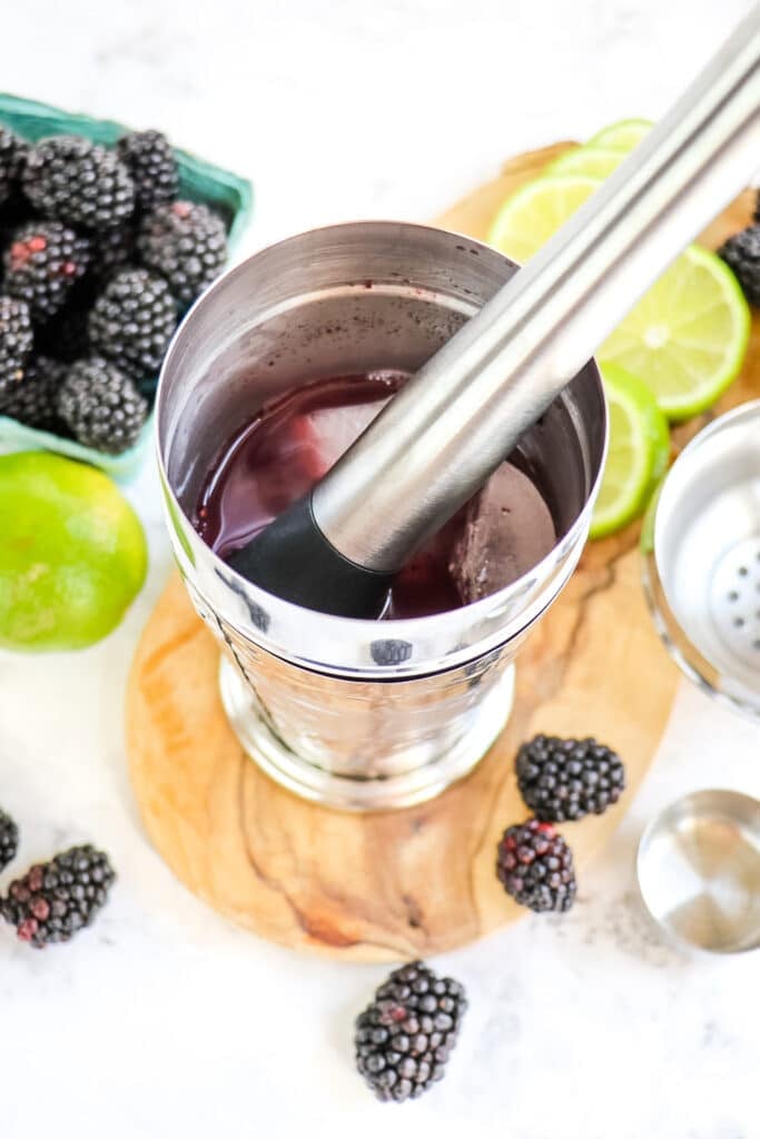 Blackberries being muddled in a cocktail shaker for a blackberry margarita.