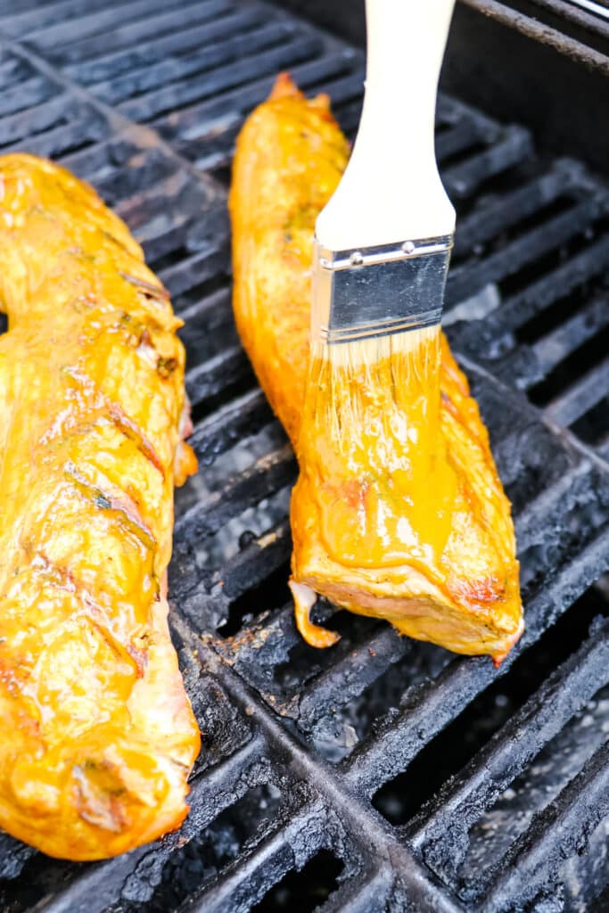 Carolina gold sauce being brushed over pork tenderloin on grill.