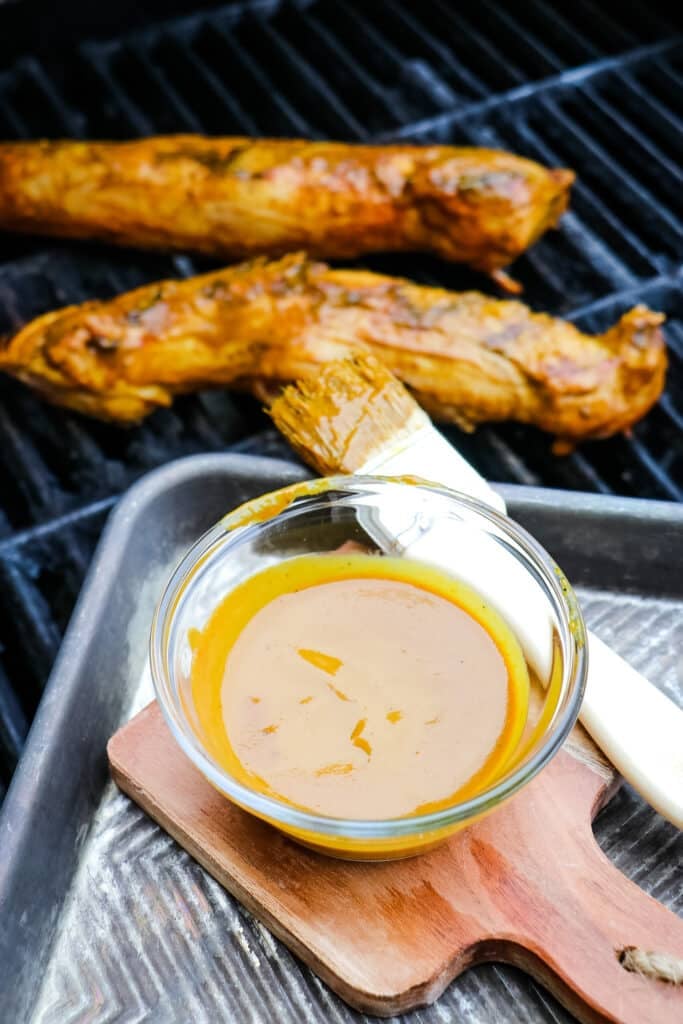 Carolina gold sauce in small bowl next to grill brush and grill.