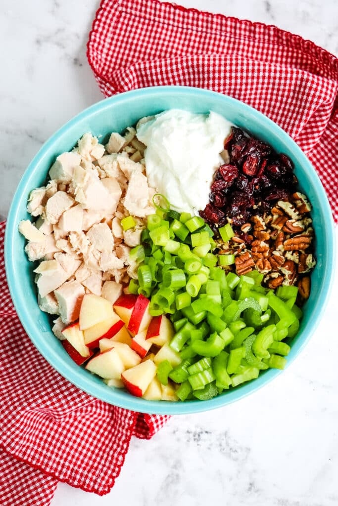 Ingredients for apple pecan chicken salad separated into sections in a blue bowl.