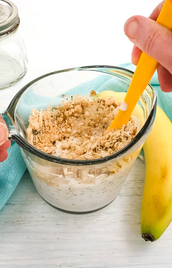Peanut butter banana overnight oats being mixed together with a rubber scraper.