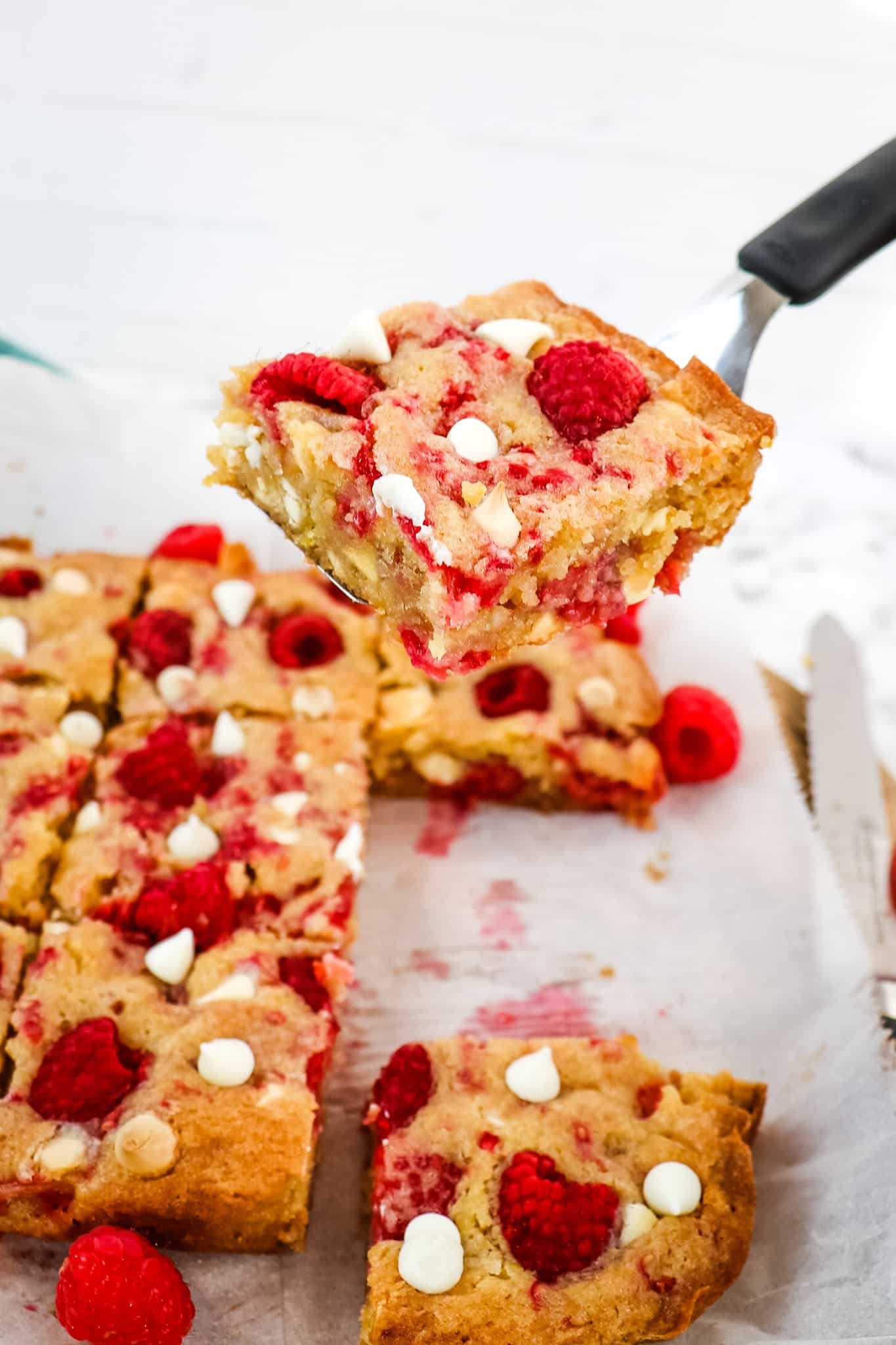 Raspberry white chocolate blondie lifted up on a spatula.