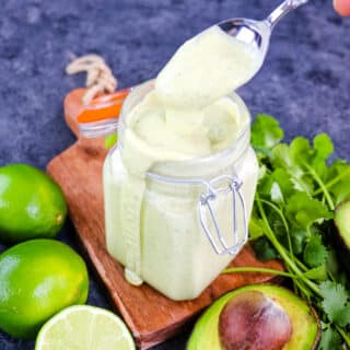 Avocado lime dressing in a jar with a spoon taking dressing out of the jar.