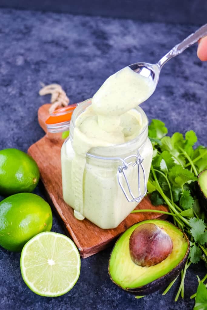 Avocado lime dressing in a jar with a spoon taking dressing out of the jar.