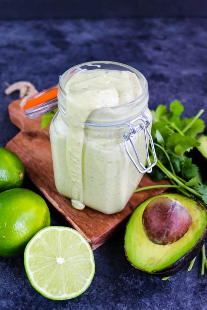 Avocado cilantro lime dressing in a jar with lime, avocado and cilantro on the side.