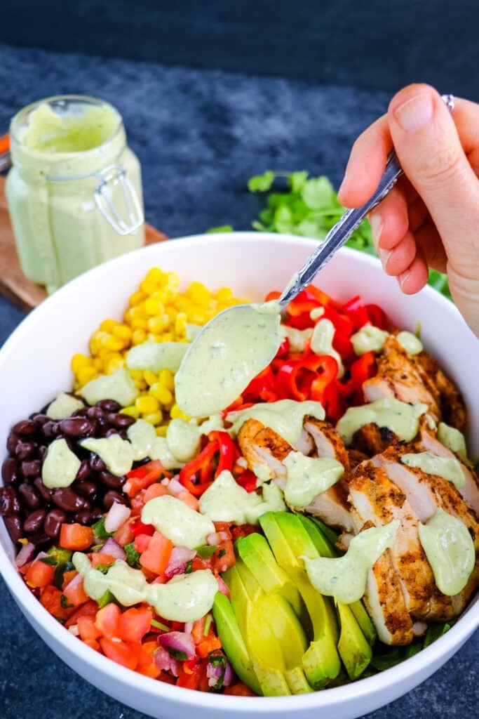 Avocado lime ranch dressing being spooned over southwest chicken salad.