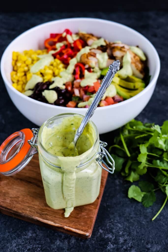 Jar of avocado lime dressing in front of a southwest chicken salad.