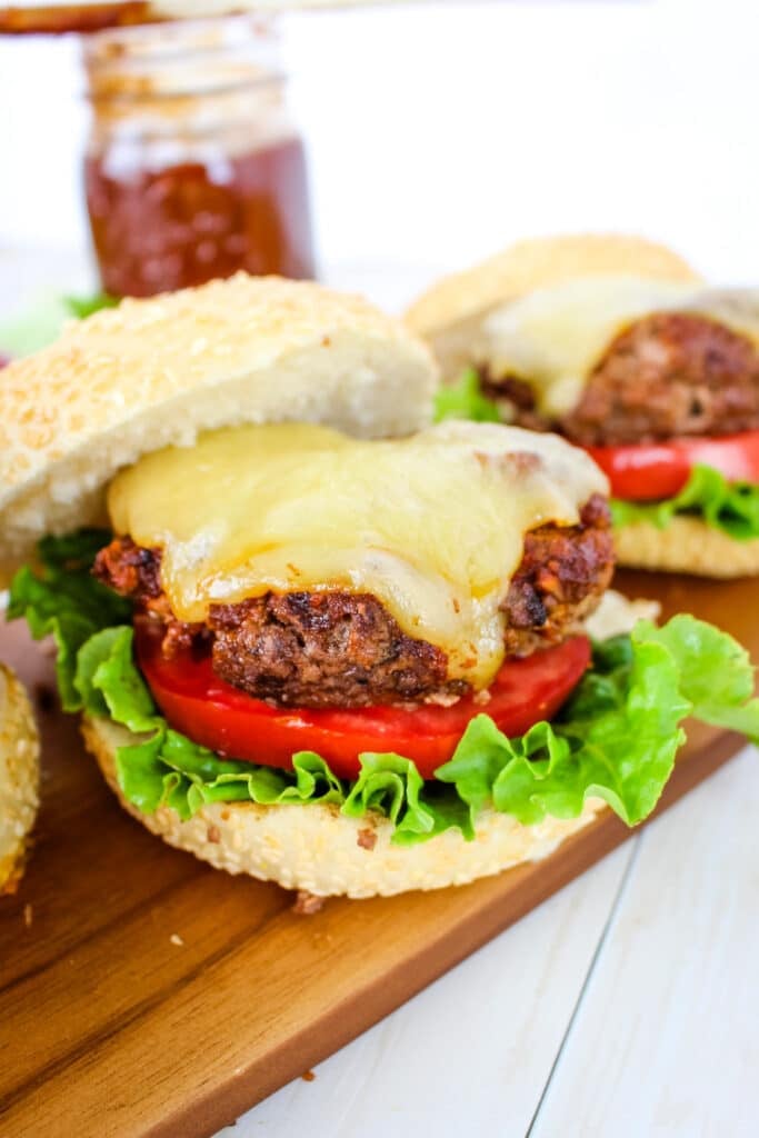 BBQ hamburger topped with a slice of melted cheese, stacked on a sesame bun with lettuce and tomato.