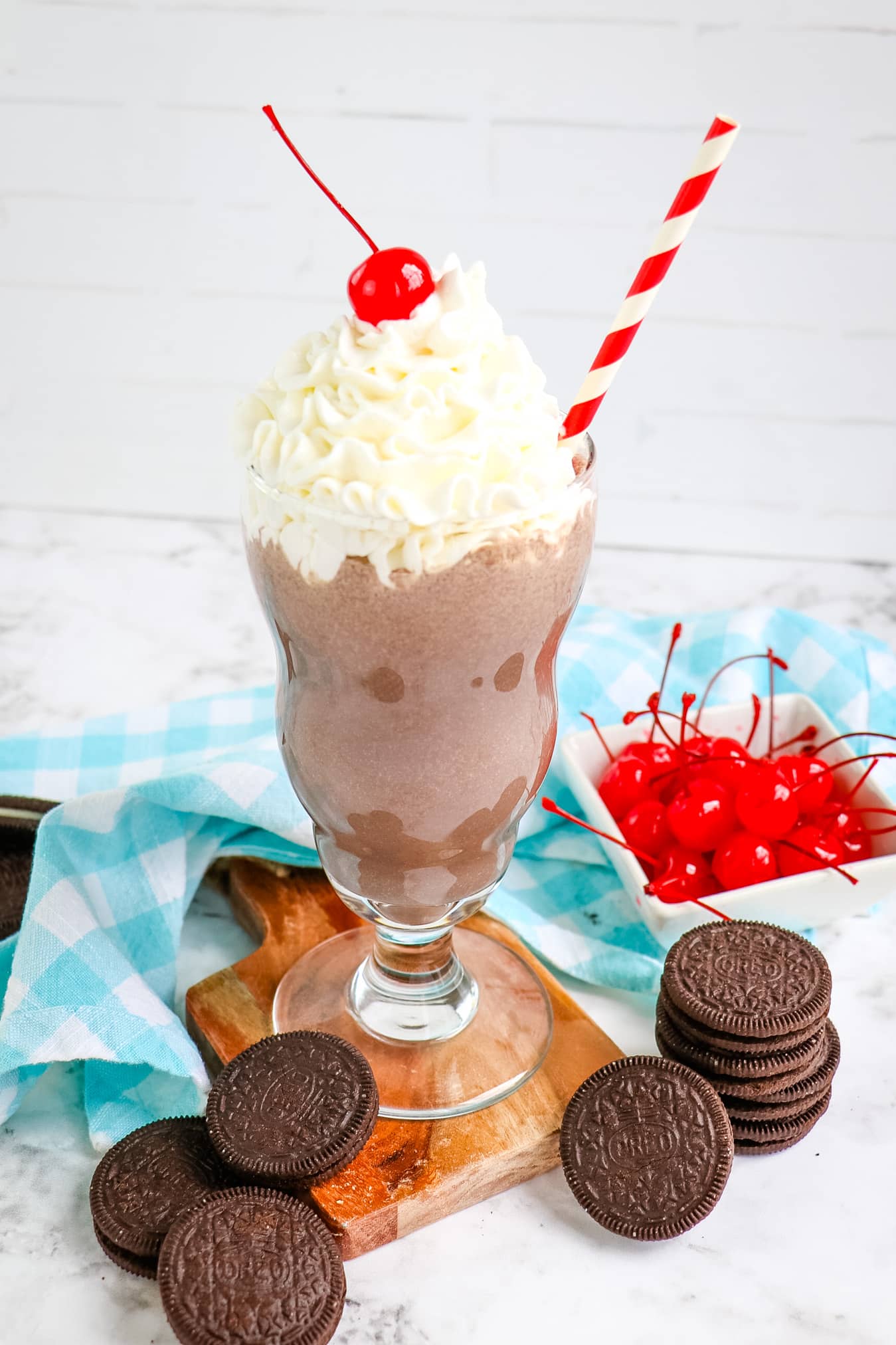 Chick fil a OREO milkshake in glass with OREO cookies and maraschino cherries on the side.