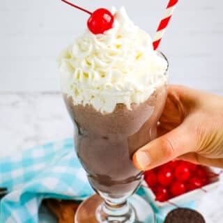 Chick fil a cookies and cream milkshake held in hand and topped with whipped cream and a cherry.