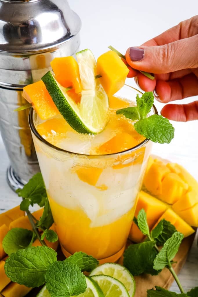 Topping a mango mojito with a garnish of mango chunks, lime slice and mint leaves.