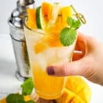 Mango mojito recipe in a glass and held in hand.