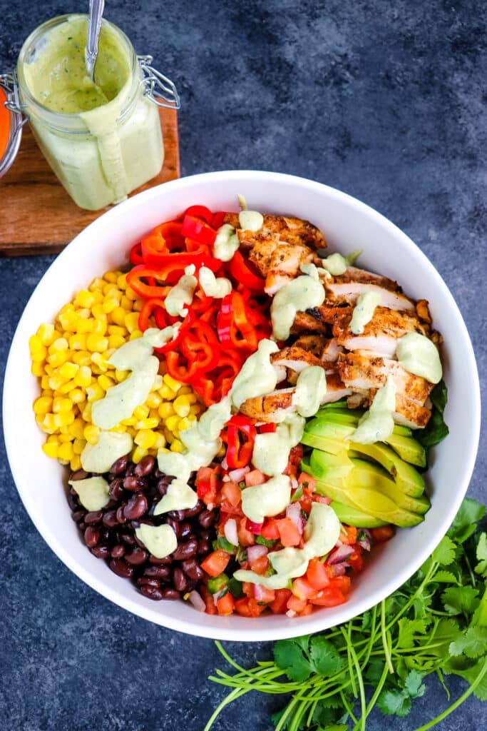 Spicy southwest chicken salad in a bowl topped with avocado ranch dressing and cilantro on the side.