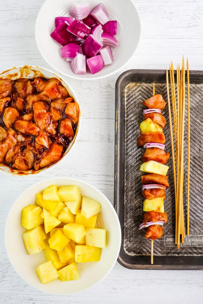 Ingredients in bowls for chicken pineapple kabobs, with one kabob assembled on a skewer.