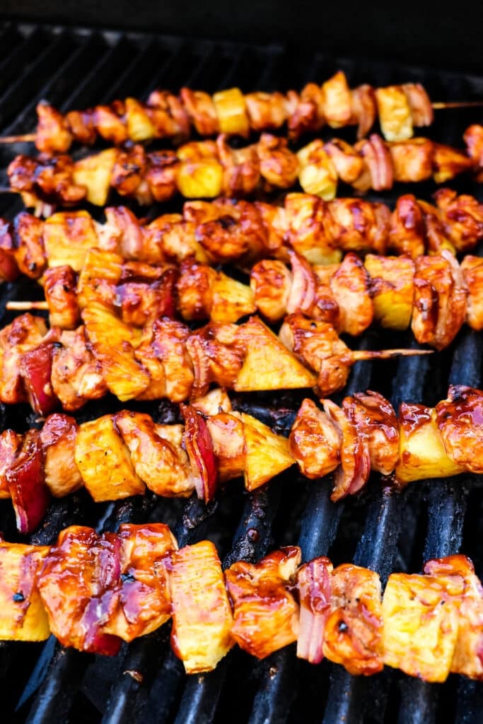 BBQ chicken kabobs with pineapple cooking on a grill.