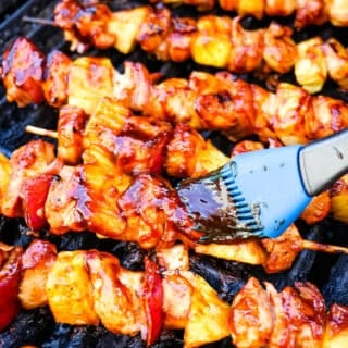 BBQ chicken skewers on the grill being brushed with barbecue sauce.