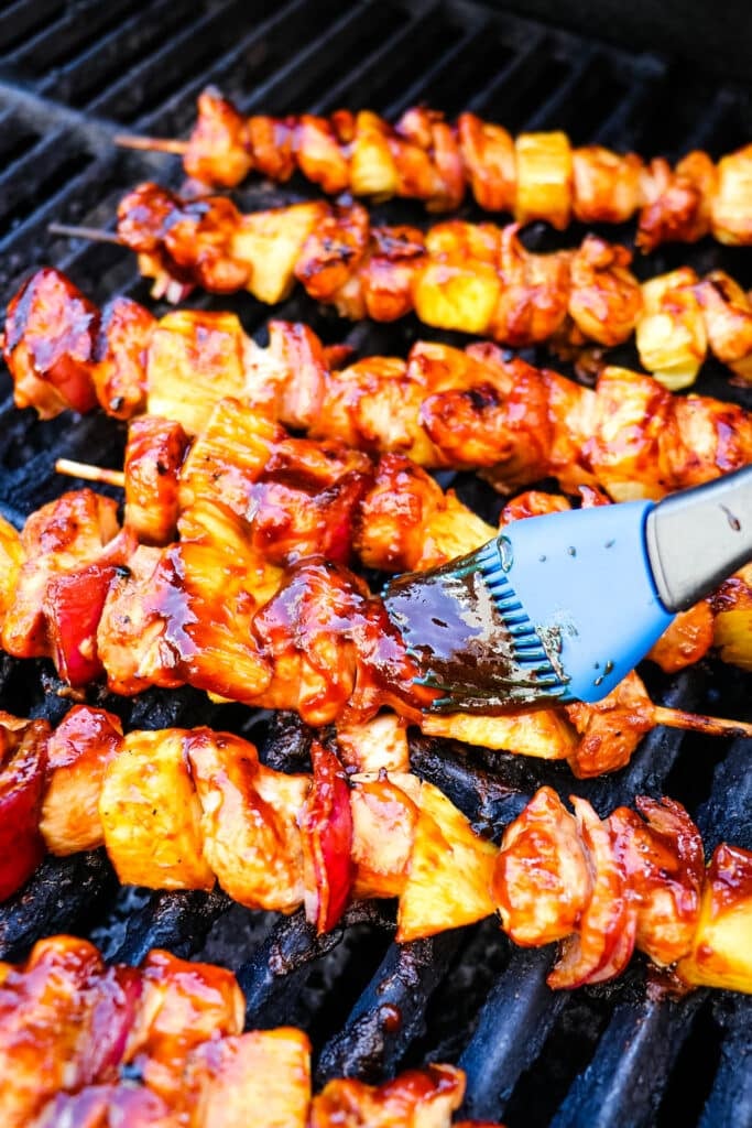 BBQ chicken skewers on the grill being brushed with barbecue sauce.