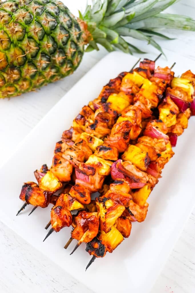 Chicken pineapple kabobs on a white platter with a pineapple in the background.