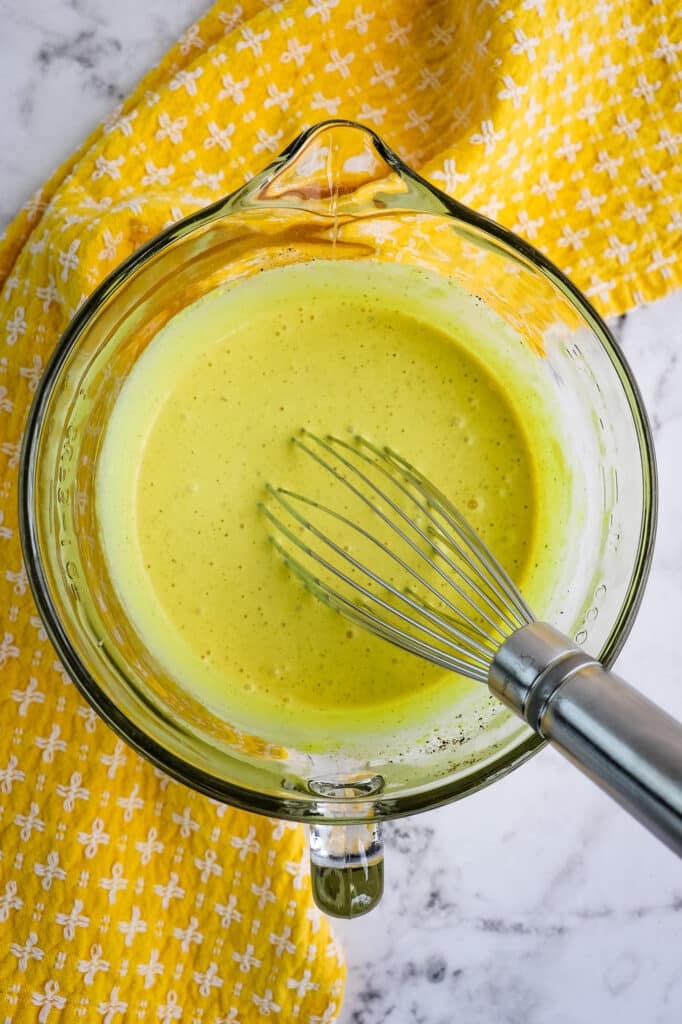 Mustard based dressing for bacon and egg potato salad, in a bowl with a whisk.