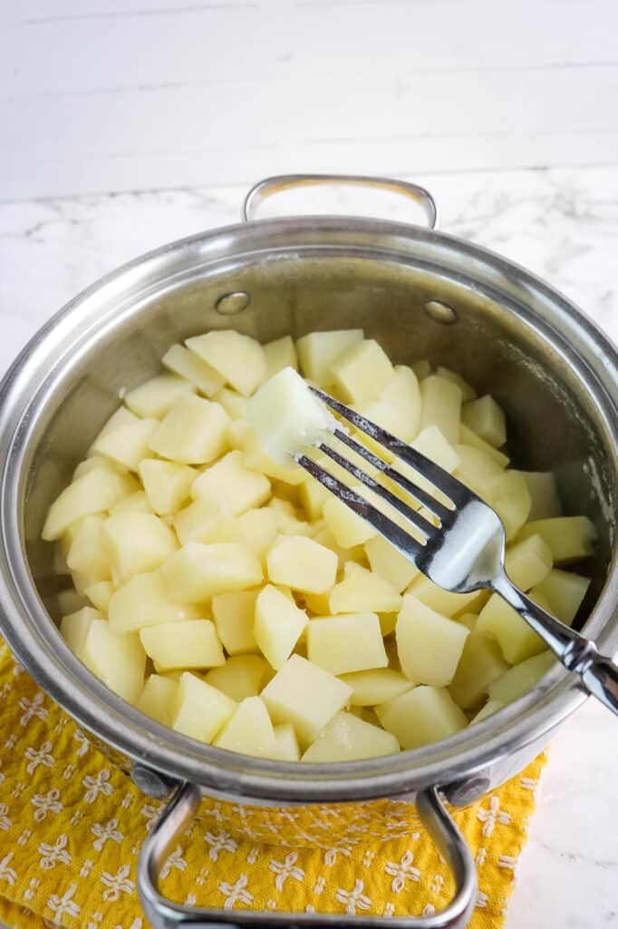 Cooke potatoes in a sauce pan with fork testing doneness of potatoes.