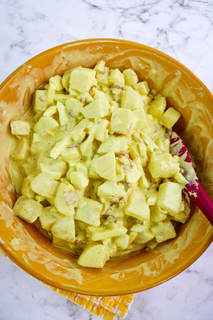 Egg potato salad in a bowl mixed together with the mustard dressing.