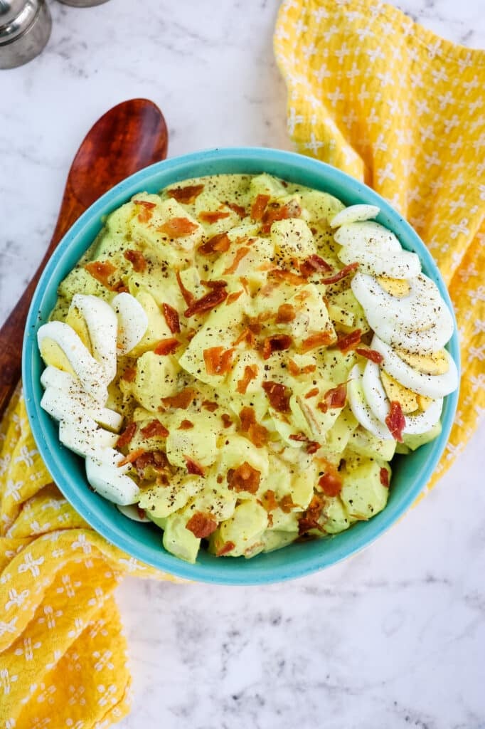 Deviled egg potato salad in a bowl, garnished with hard boiled eggs, bacon bits and ground pepper.