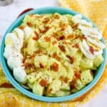 Deviled Egg Potato Salad topped with bacon bits, eggs and ground pepper.