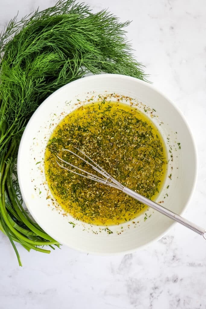Lemon olive oil salad dressing in a bowl with dill on the side.