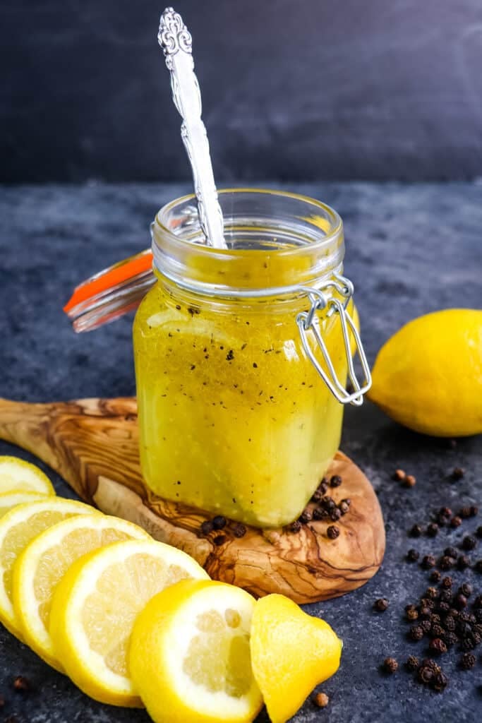 Lemon olive oil dressing in a small jar with a spoon in the jar and sliced lemons on the side.