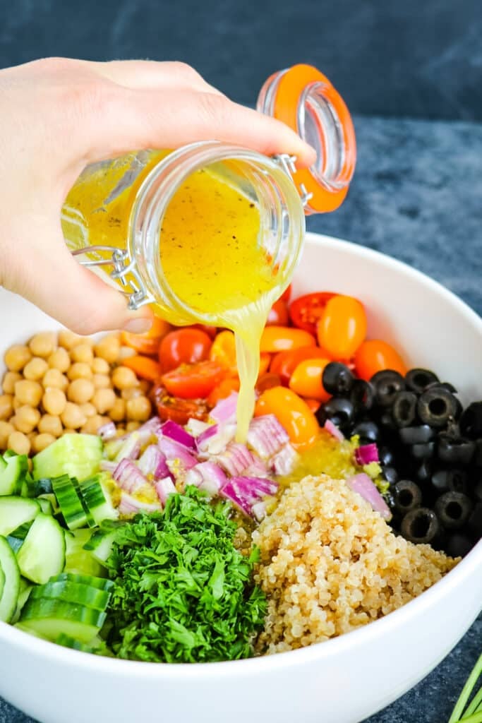 Lemon olive oil salad dressing being poured from a jar on to quinoa chickpea salad.