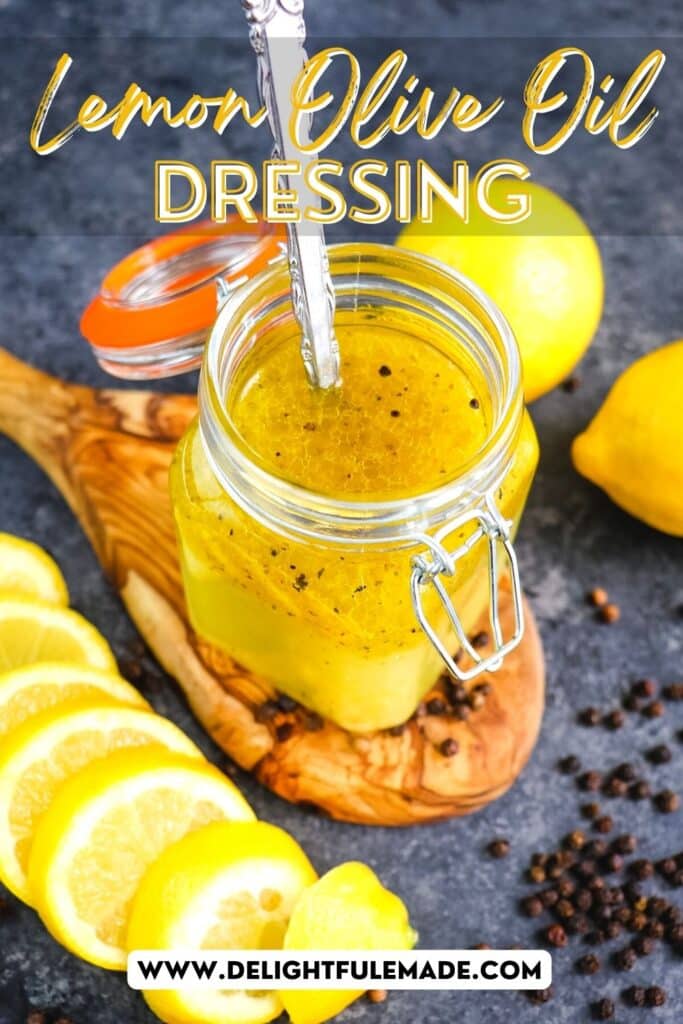 Lemon olive oil dressing in a small jar with lemon sliced and peppercorns on the side.