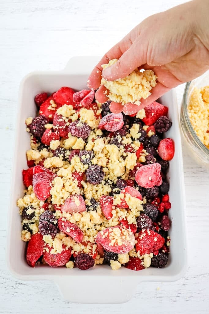 Topping frozen berries in baking dish with cake mix crumble for a mixed berry cobbler with cake mix.