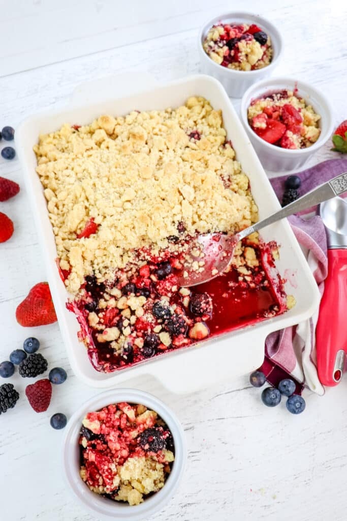 Berry cobbler with cake mix with servings in three individual bowls, with berries on the side.
