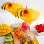 Two mango daiquiri's with lime and mango slices and maraschino cherries on the side.