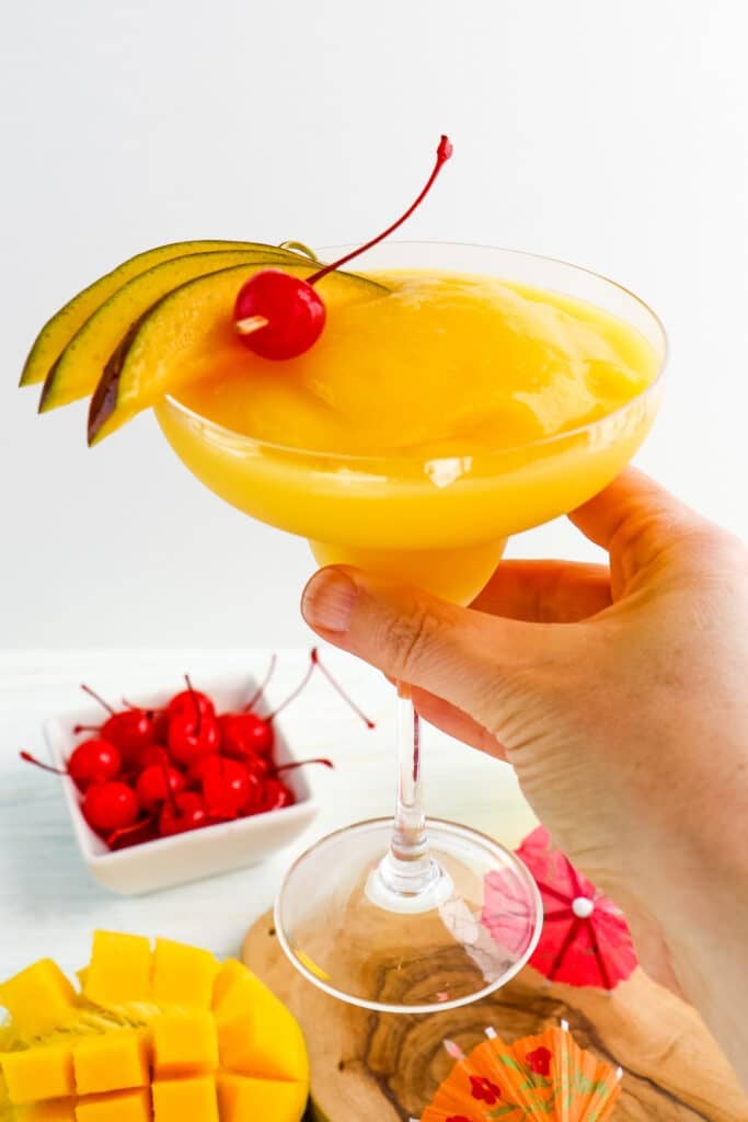 Frozen mango daiquiri recipe in a glass and held in hand.