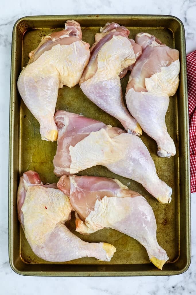 Chicken leg quarters on a sheet pan trimmed of excess fat.